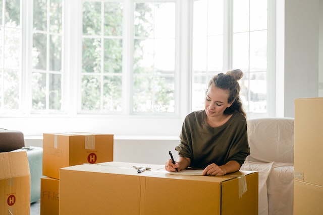 a tenant in a green crewneck sweater smiles while labelling a moving box to prepare to move out of their rental home